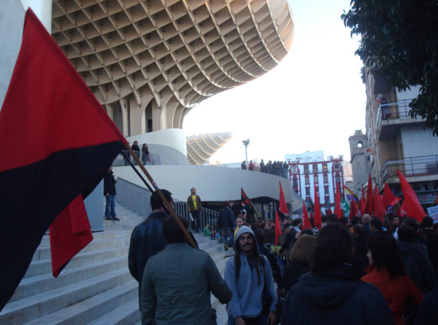 Protesters in Seville carry the anarchist red and black flag past Las Setas, 'The Mushrooms', January 2012
