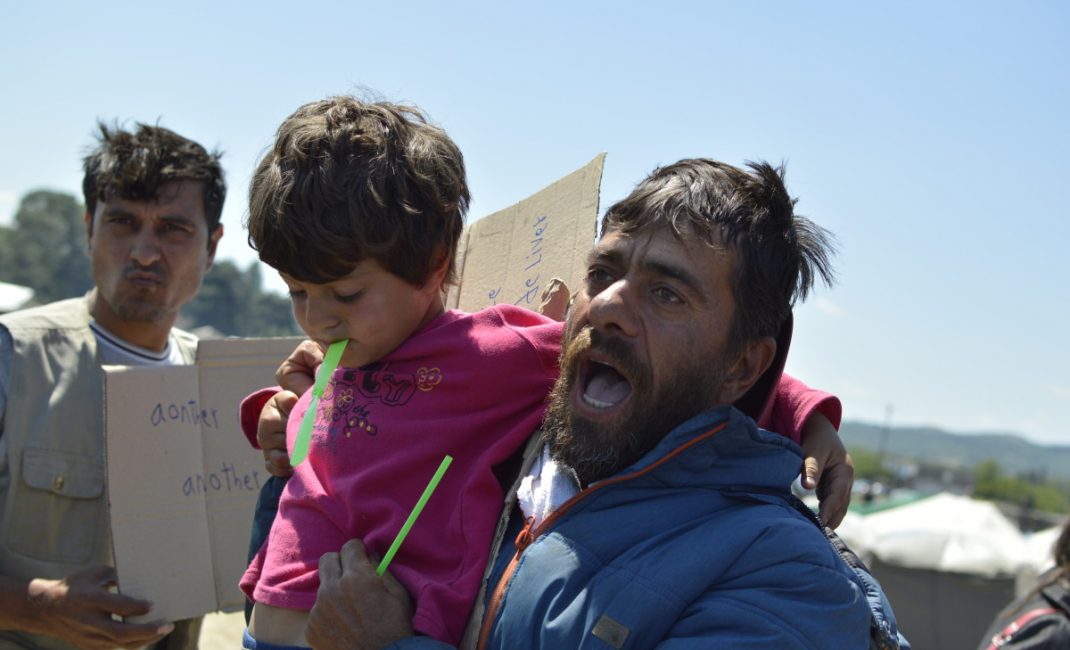 A refugee address other Idomeni refugees during a manifestation holding his child