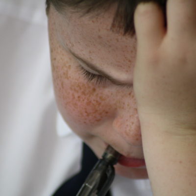 Boy in school uniform chews his pen as he frowns down at his work with his head in his hand. GCSE stress.