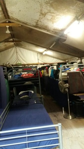A cramped, dirty tent on Nauru crammed with bunk beds under fluorescent strip lights.
