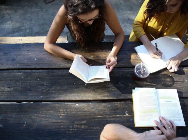 Three girls writing in separate notepads on a bench outdoors