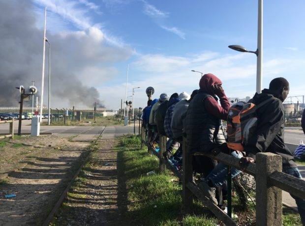 It Can Be Done migrant law podcast - a row of refugee men sitting on a fence by a railway track