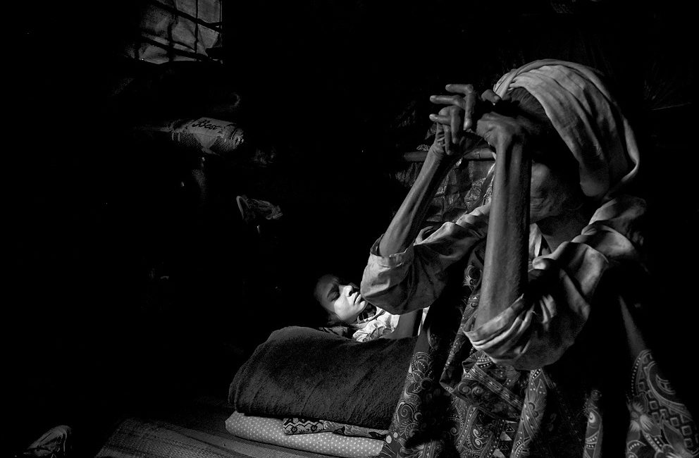 A great proportion of the Rohingya population living in the camps suffer from underlying health conditions. Due to the Covid-19 restrictions, healthcare support has been drastically reduced. In the image a mother takes care of her disabled daughter in their makeshift hut in the Kutupalong Refugee Camp - by Francesc Galban