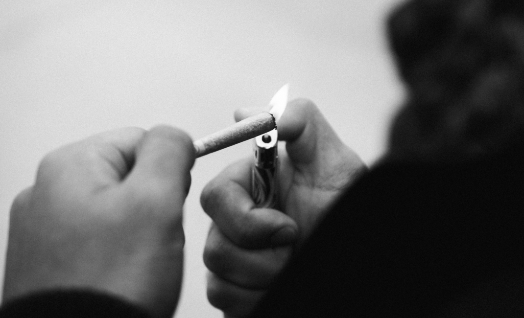 black and white photo showing close-up of hands lighting a hand-rolled cigarette