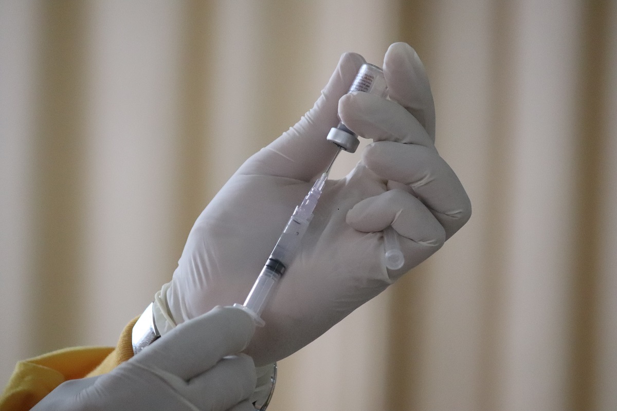 Hands in surgical gloves handle a syringe and vaccine vial