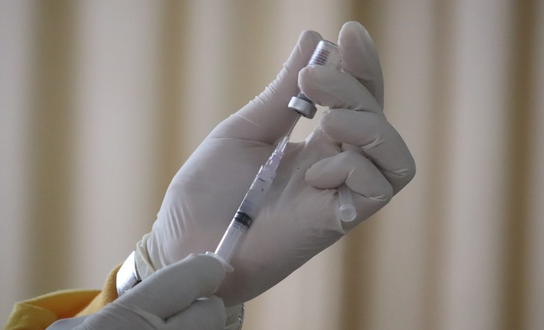 Hands in surgical gloves handle a syringe and vaccine vial