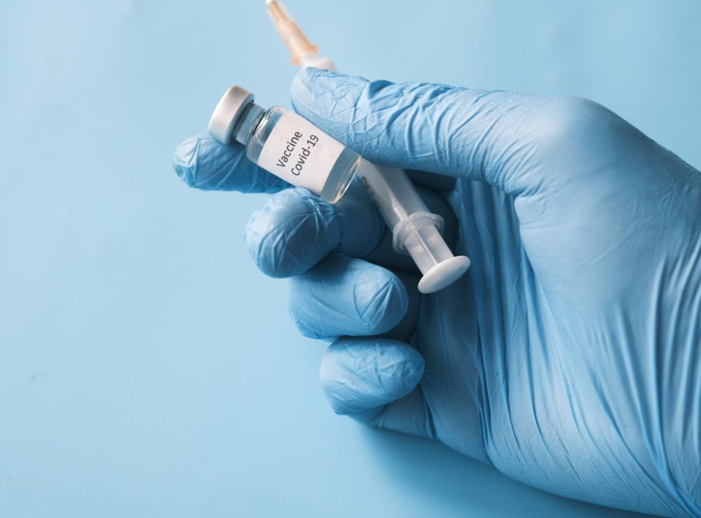 Hand with medical glove holding a COVID-19 Vaccine and a needle