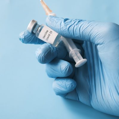 Hand with medical glove holding a COVID-19 Vaccine and a needle