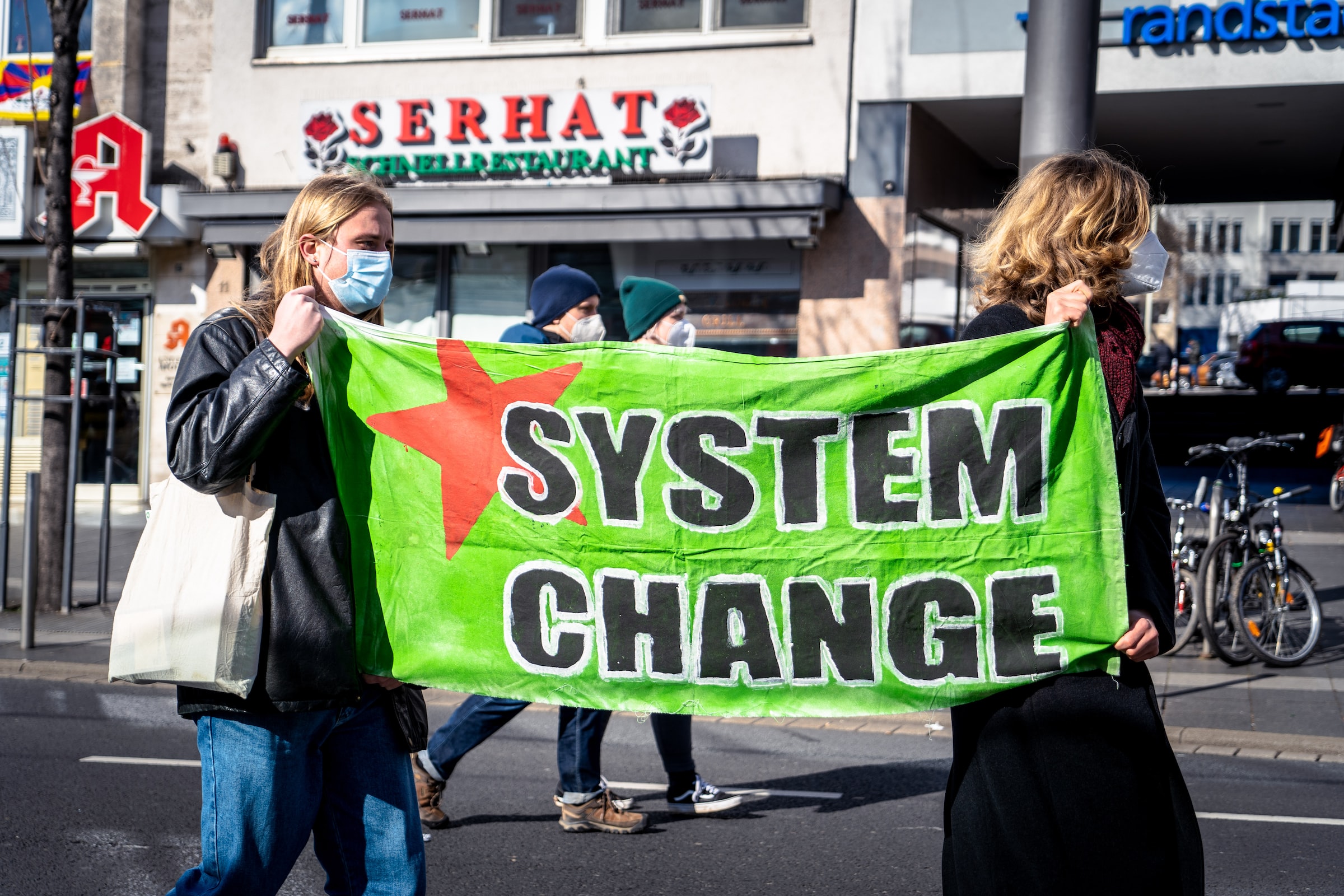 Two people holding a green banner that says "System Change" with a red star behind it