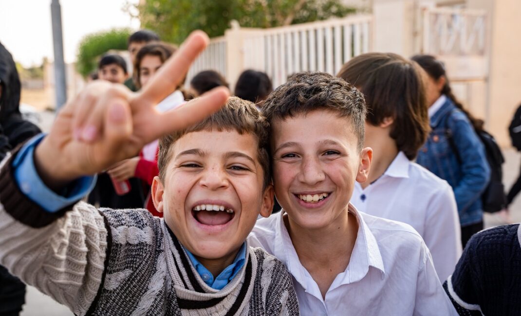 two boys laughing at the camera, one shows the 'Victory' sign