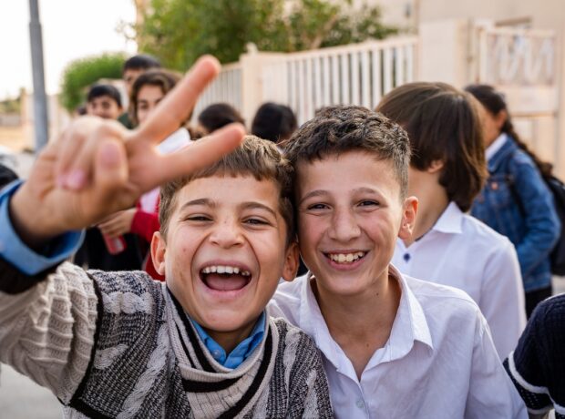 two boys laughing at the camera, one shows the 'Victory' sign