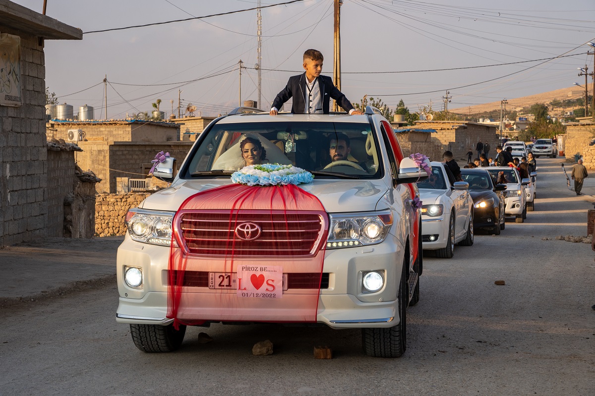 a car, specially decorated for a wedding with a bride and a groom in it: a boy stands in the car, looking through the roof