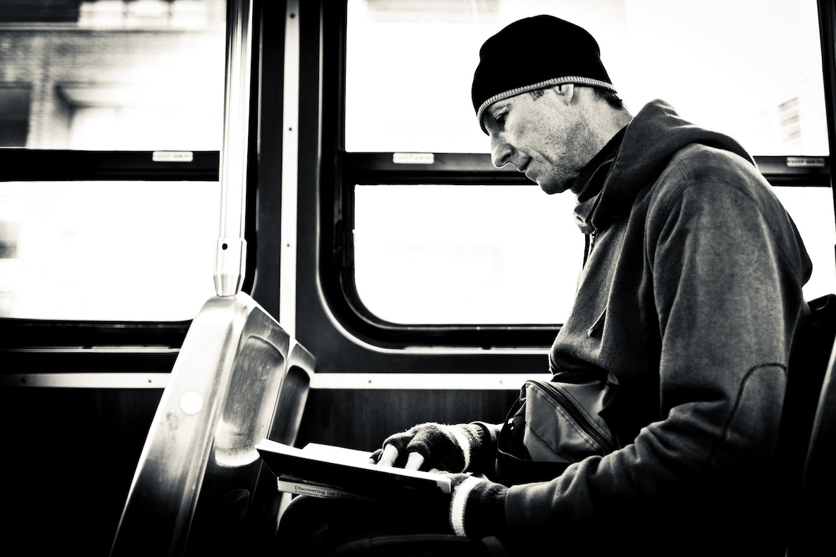 black and white picture featuring a man with a beanie holding a book in his hands in a train