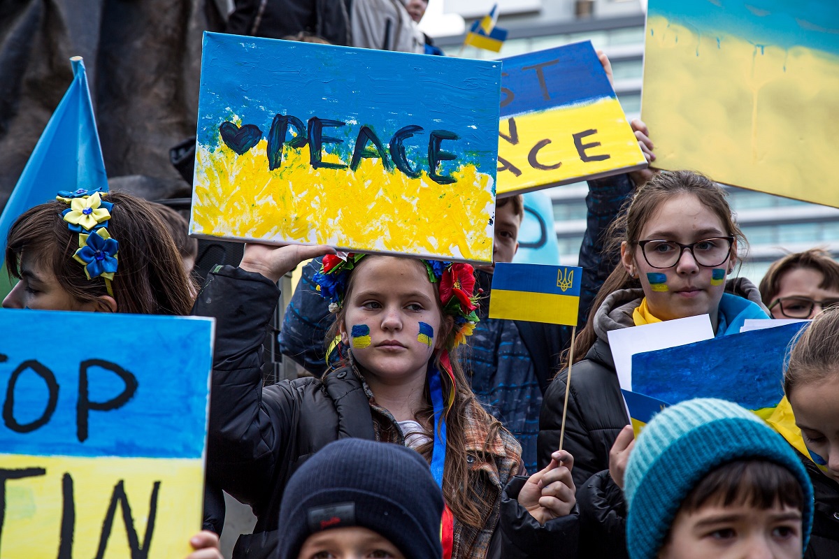 Photograph showing a crowd of people holding 'peace' signs in blue and yellow