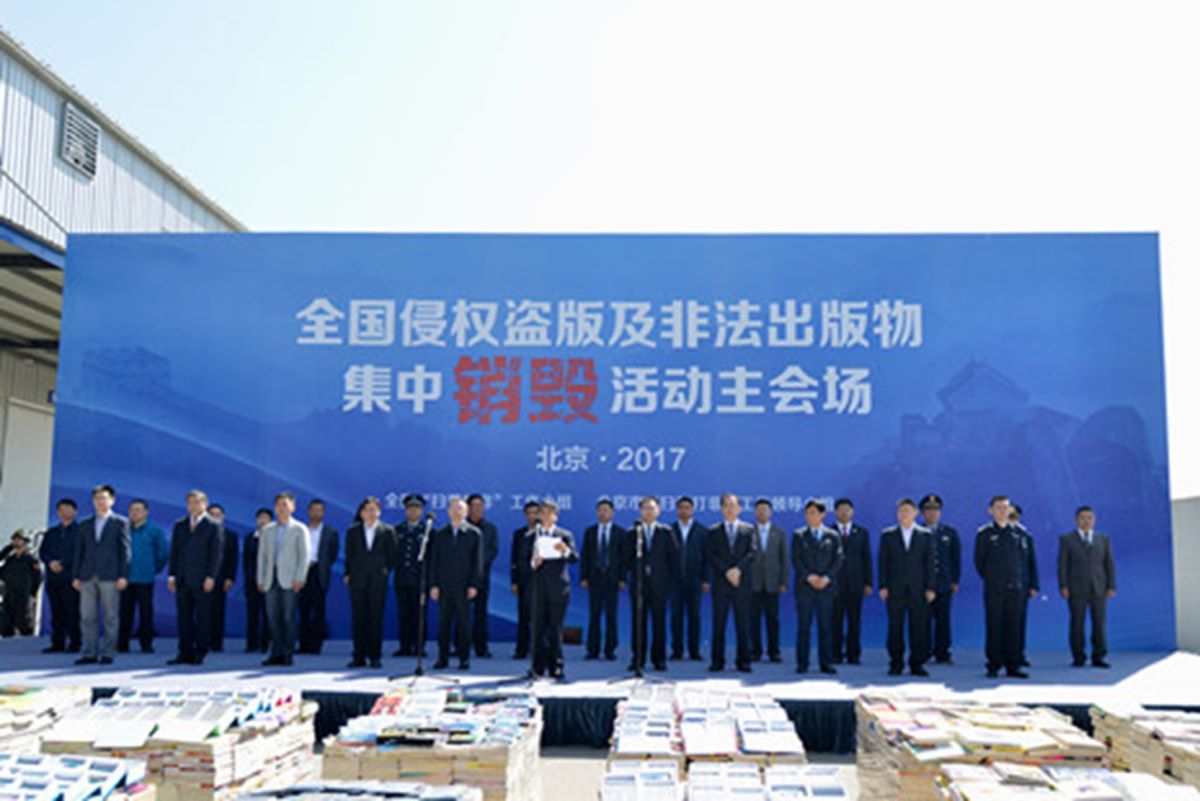 A group of men stood in front of a big blue sign and behind a piles of hundreds of books