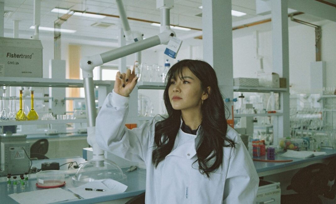 woman in white medical scrub looking at a bottle in a lab