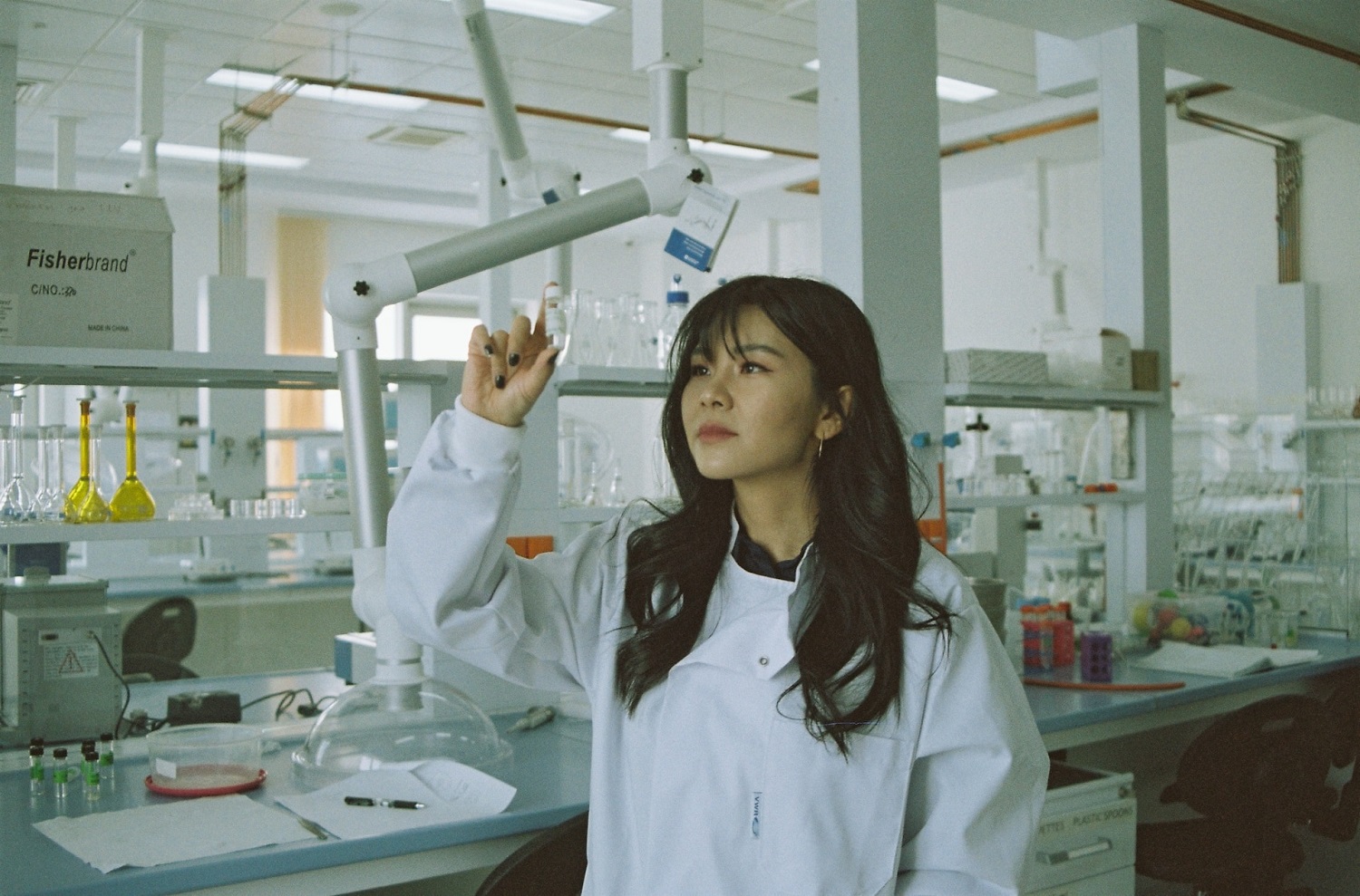 woman in white medical scrub looking at a bottle in a lab