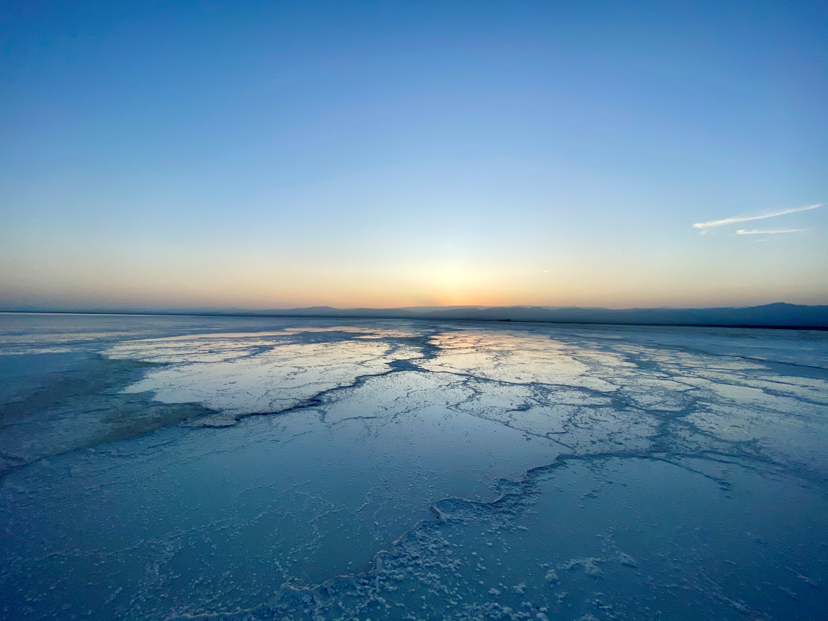 A wide shot of the salt lake. Salt formations crystallise on the top of the lake as the sun sets in a blue sky