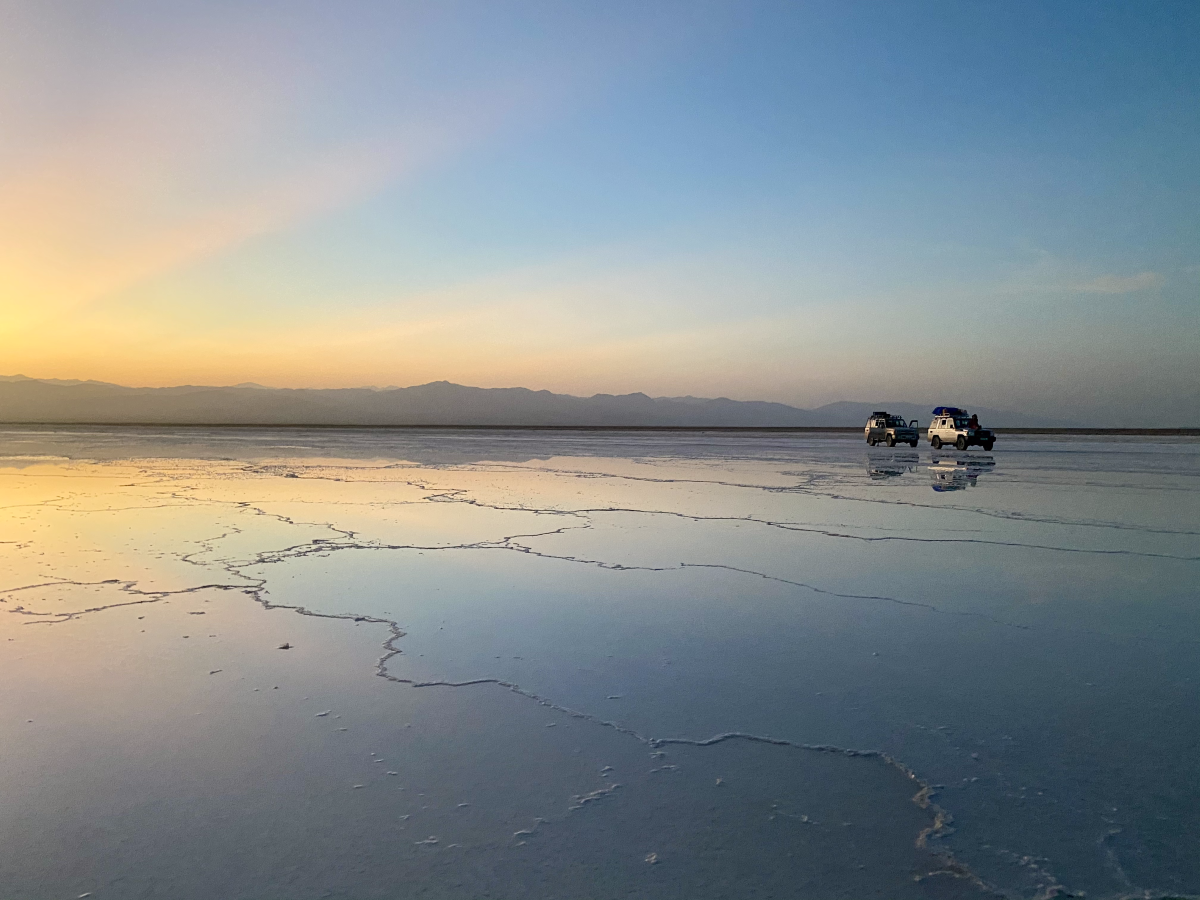 Trucks are stationed in the distance of the salt lake as the sun sets in the background
