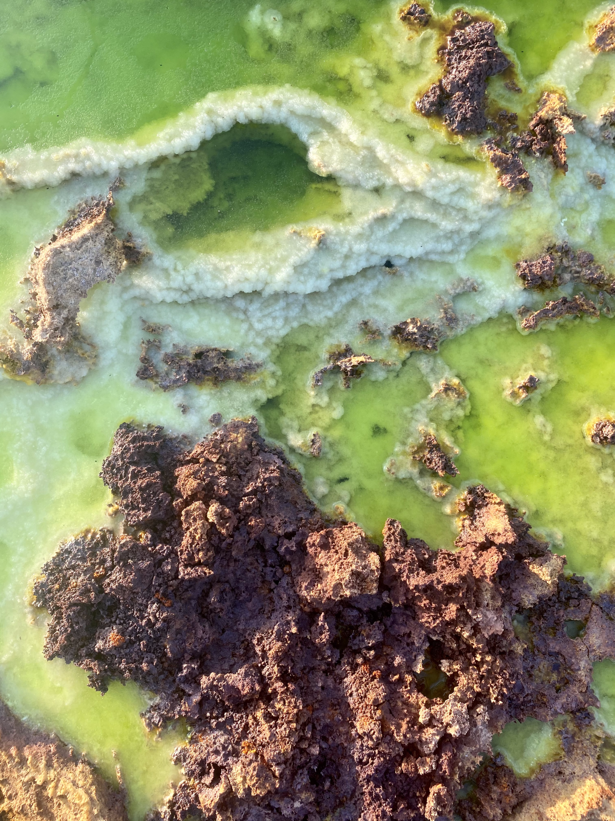 A close-up of a pond filled with clear greenish yellow liquid, white, layered crystallised formations, and rock-like clusters