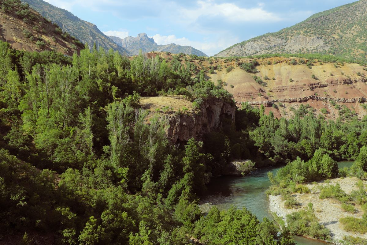 Lush cliffs and trees surround a river. The sky is blue with scattered clouds 