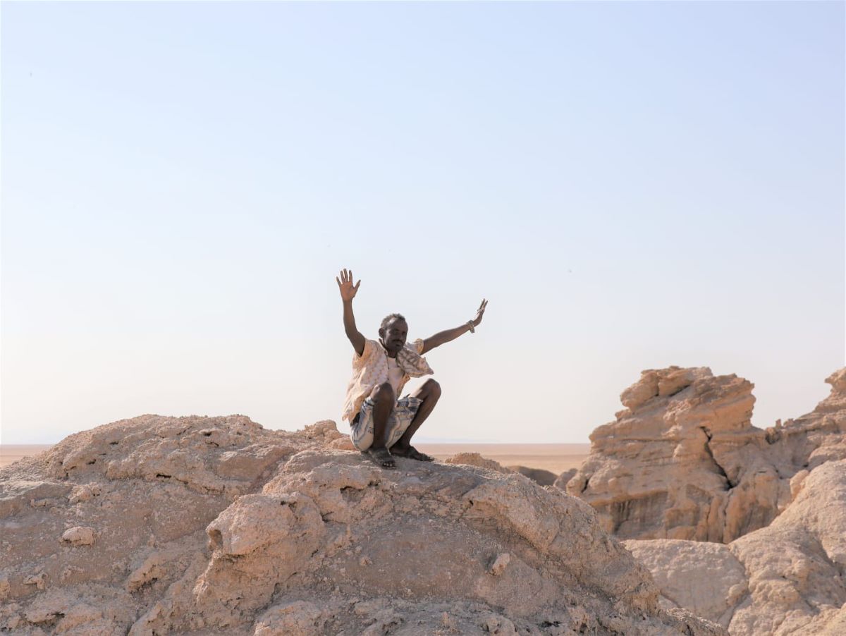 Aboubakr sits atop a large rock structure with his arms raised to the sky