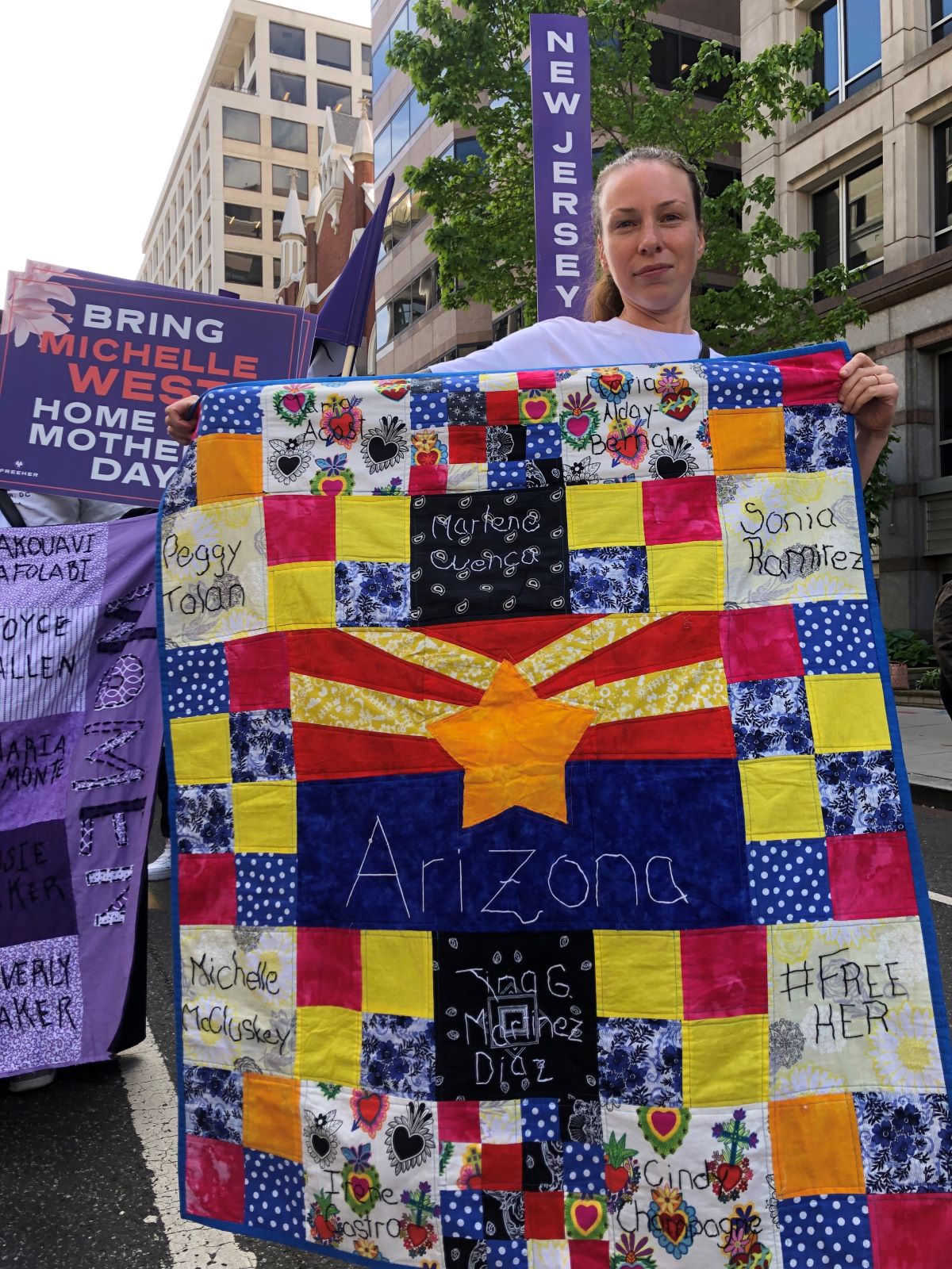 A woman proudly holds a quilt which reads "Arizona" in the middle with the names of various woman inmates on some of the quilt's squares