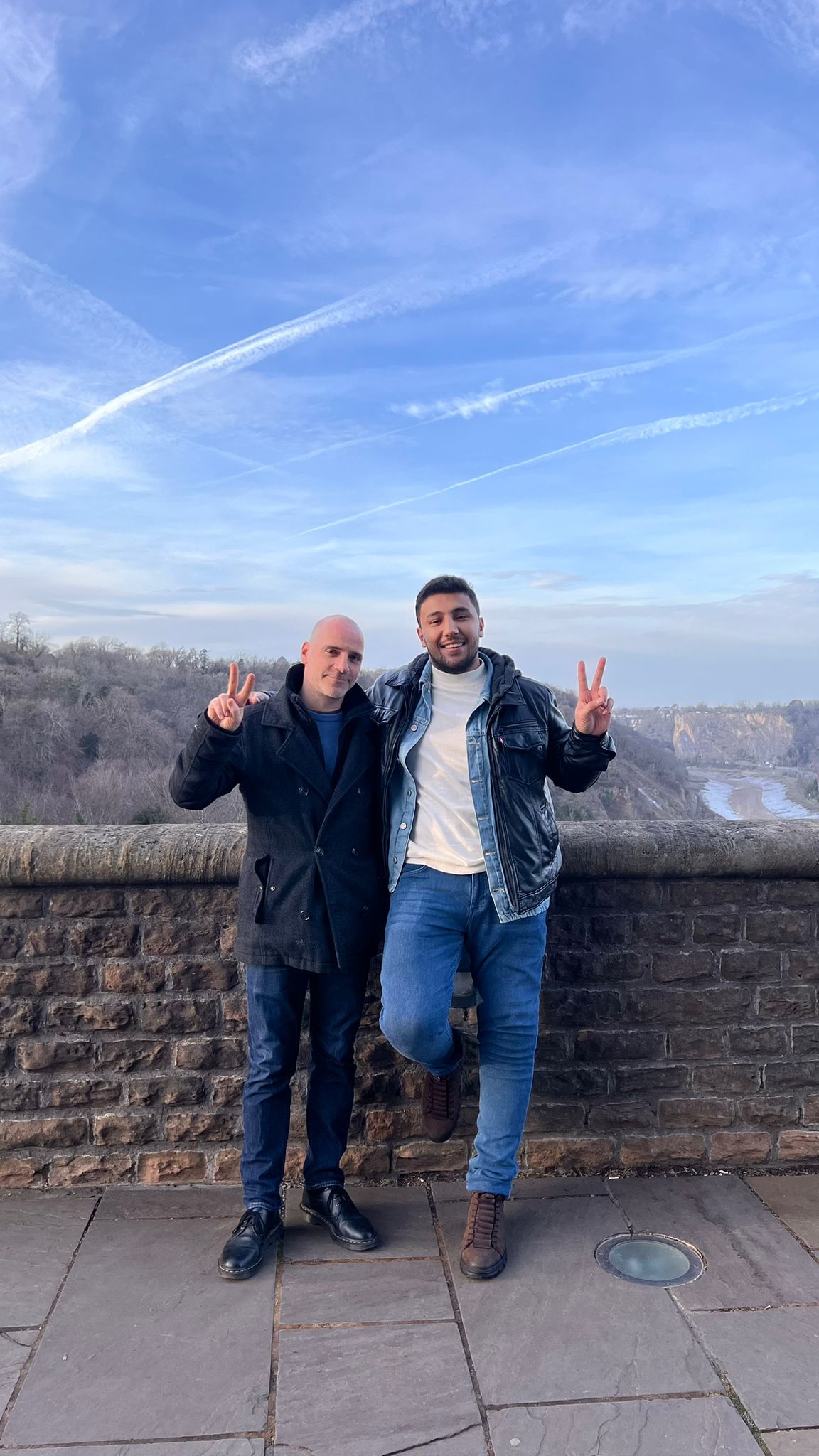 Ronnie Barkan and Mohammed Al Zaza in Bristol. They are both holding their hands up in a peace sign with a blue, cloudy sky behind them