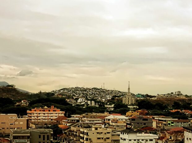 a wide angle view of the city of Guayaquil, with many buildings, a spire, and some hills in the distance