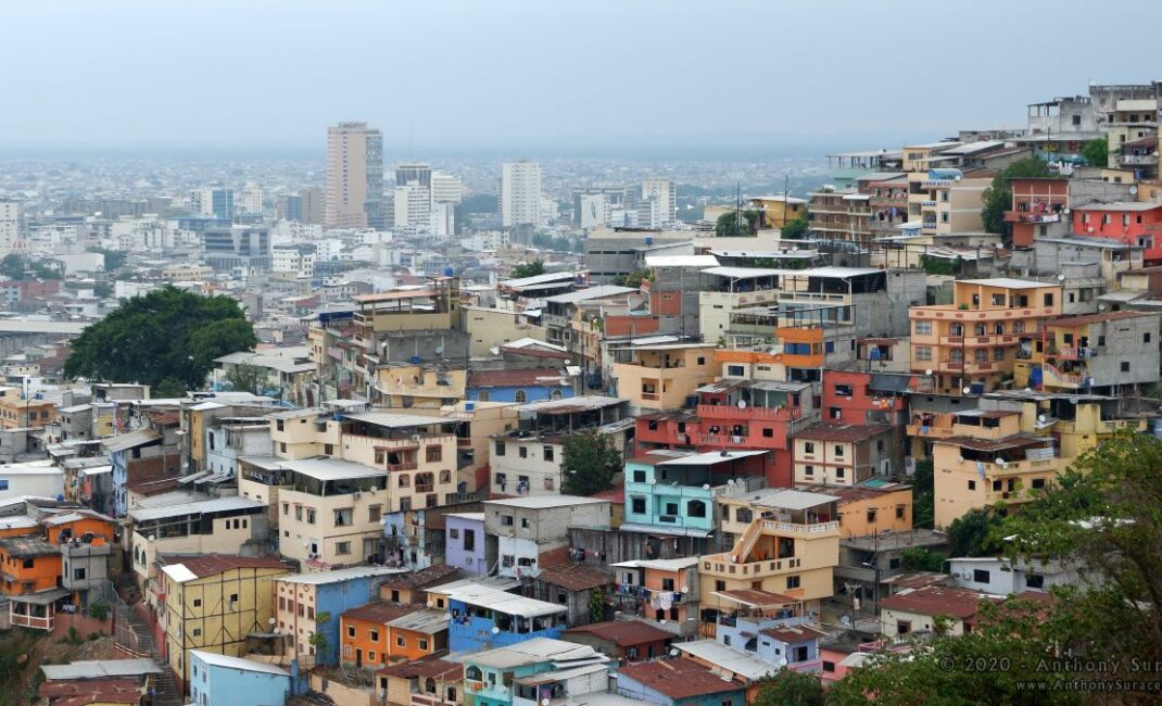 a wide aerial shot of colourful houses and apartment buildings with a city in the distant background