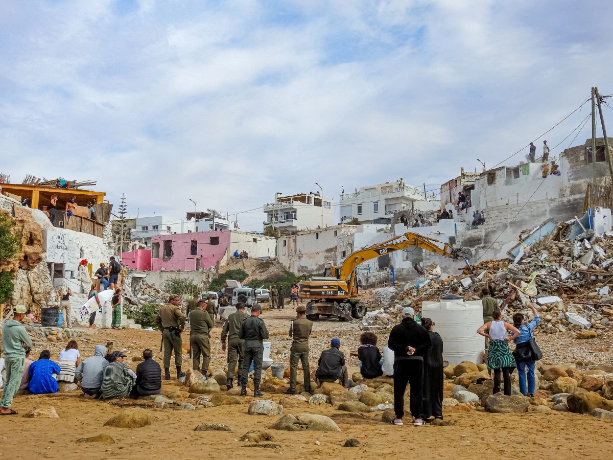 a CAT vehicle demolishes houses in the distance as a group of people watch