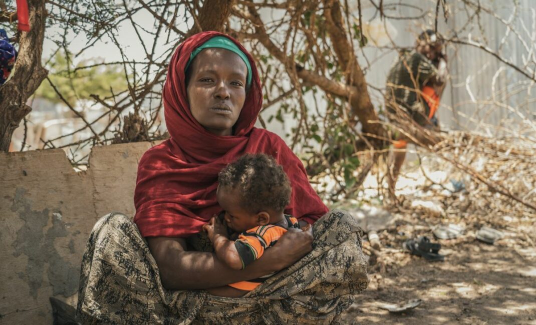 a woman sits under a tree breastfeeding a baby