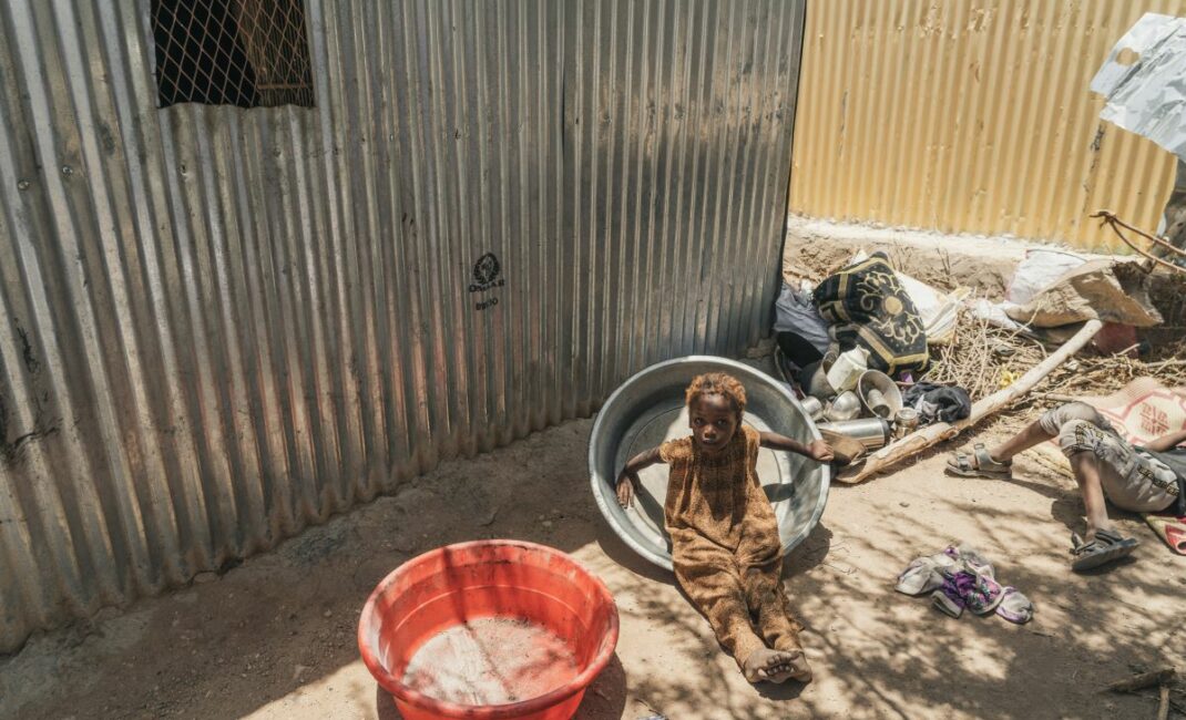 a child sits in a metal tub surrounded by clothes and belongings