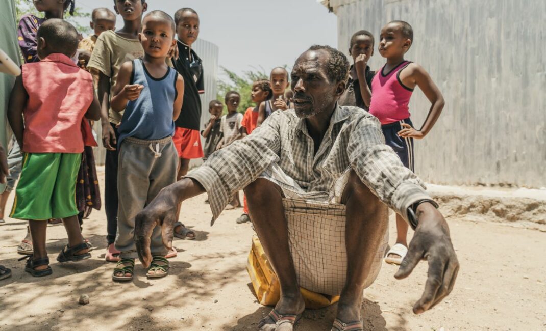 a man squats down, surrounded by children