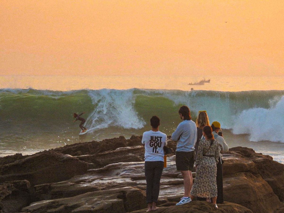 a group of people stand on some rocks and watch a person surf in the ocean