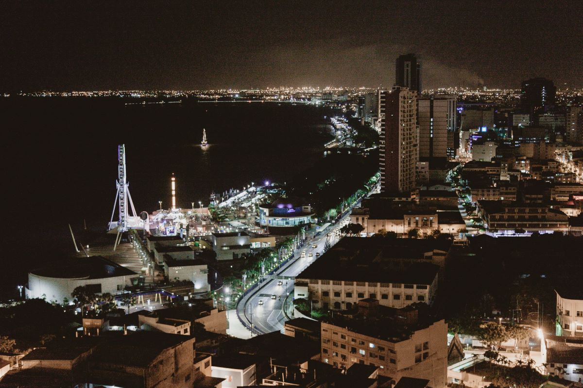 aerial photo of the city of Guayaquil at night, with the sea to the left and the buildings to the right, and a brightly lit street running along the waterfront