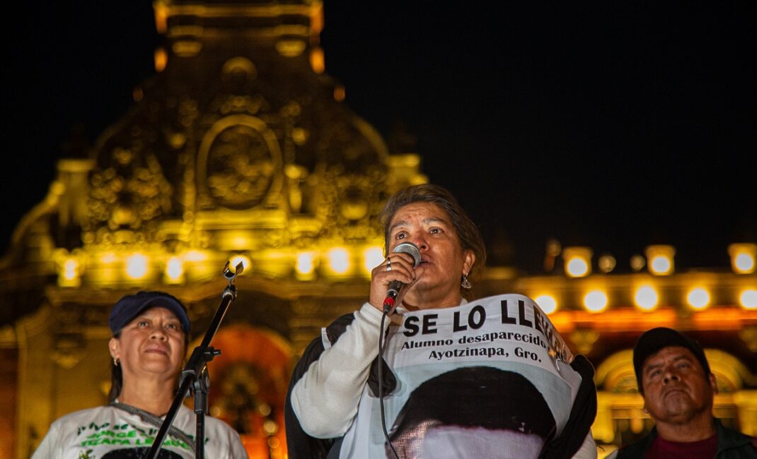 As night falls, a protester speaks into a microphone with a civic building lit up behind her