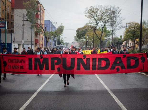 Students hold a long red banner reading "Ayotzinapa the years of impunity" - by Paula González