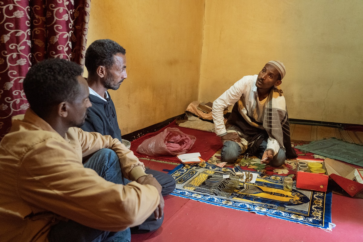 Photograph by Jaclynn Ashly showing an Ethiopian man kneeling on the floor and showing his hand to two other man, next to him is an open box with traditional medicine.