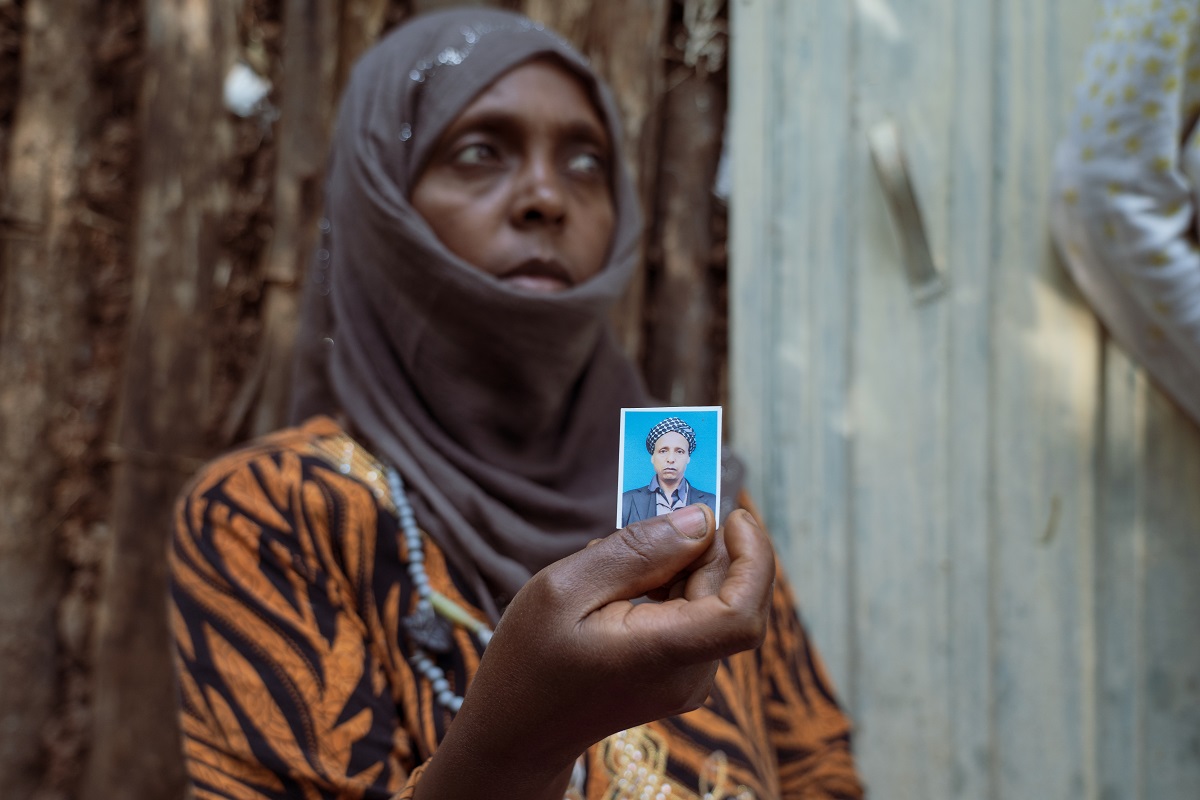  Photograph by Jaclynn Ashly showing an Ethiopian women with a black and orange stripped dress and a hijab, holding a picture of her husband who was killed.