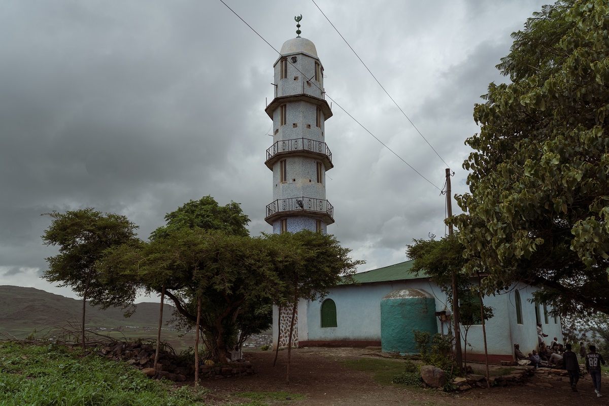 Sheikh Ali Gondar mosque with a minaret and green roof. A group of men surround the mosque's entrance on a cloudy day:  Photograph by Jaclynn Ashly for Lacuna story on religious tensions in Ethiopia.