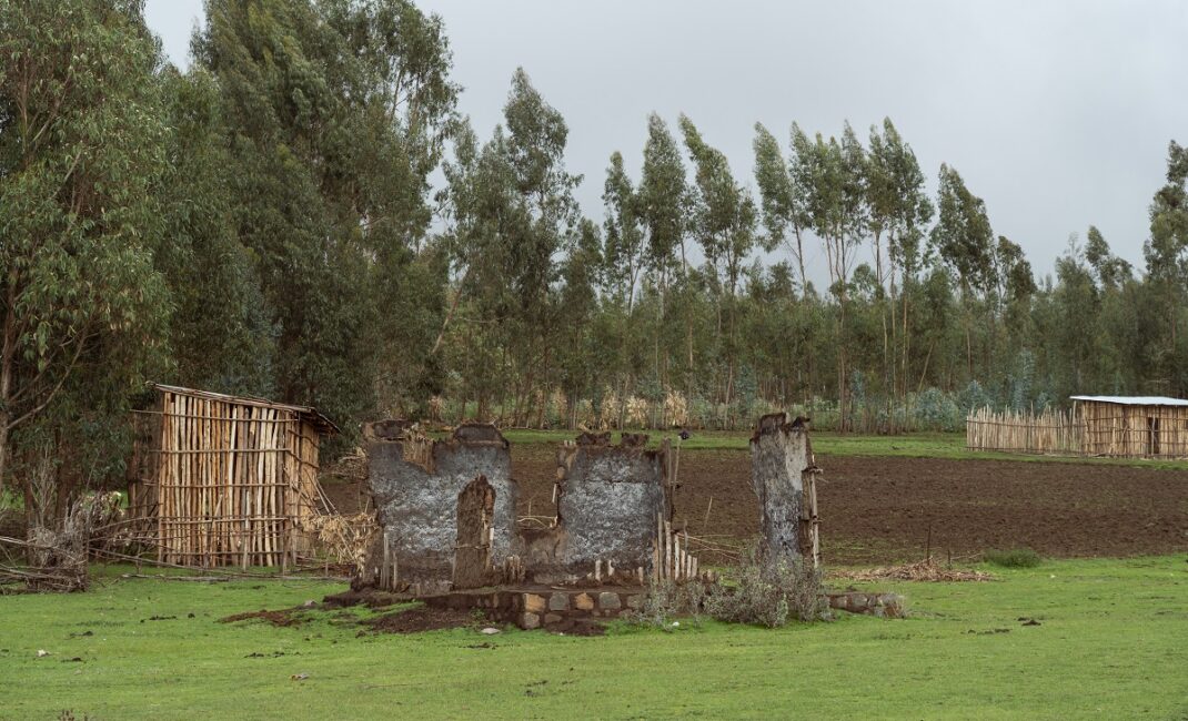 Incinerated remains of the local mosque in Debark. Trees line the perimeter, there is a muddy field and two sheds made out of branches stand:  Photograph by Jaclynn Ashly for Lacuna story on religious tensions in Ethiopia.