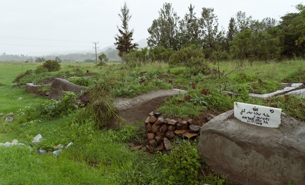 A cemetery in Sheikh Ali Gondar, Ethiopia. It is covered in growing grass, surrounded by fields, trees and litter.  Photograph by Jaclynn Ashly for Lacuna story on religious tensions in Ethiopia