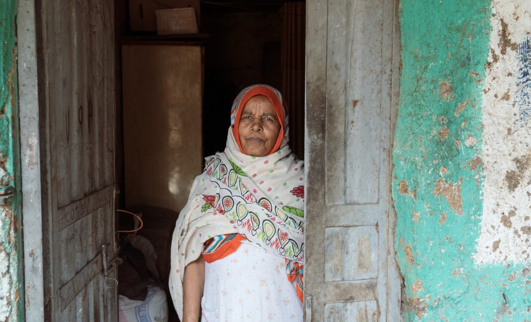 Photograph by Jaclynn Ashly showing a women with a white dress and hijab standing in front of her house in Gondar, Ethiopia