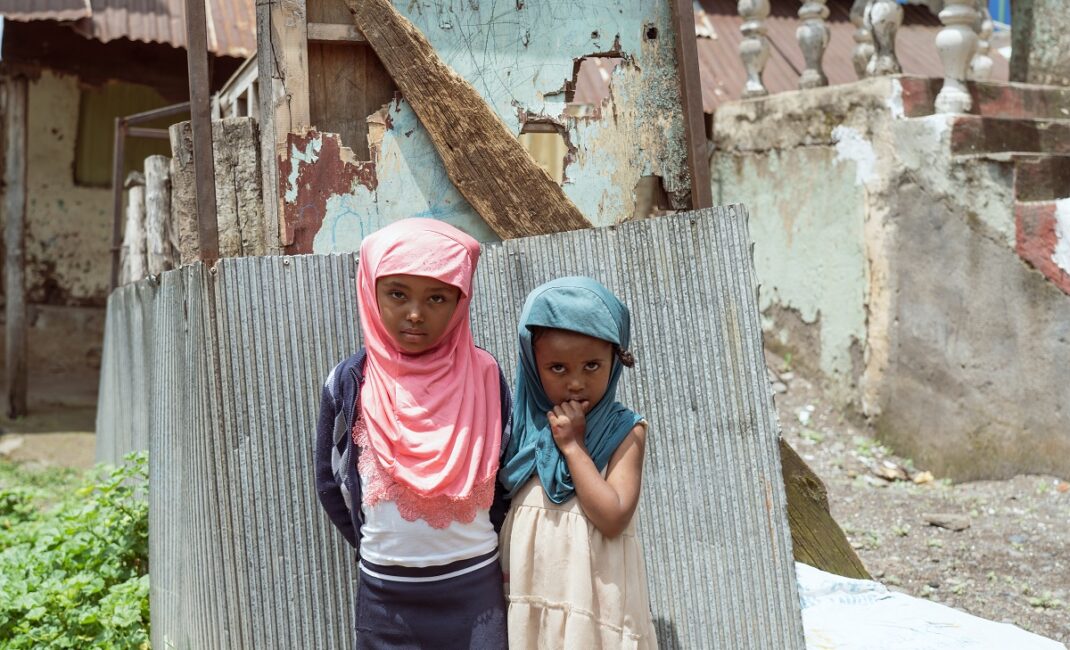 Photograph by Jaclynn Ashly showing two young girls with a colourful hijab: shack homes in the back